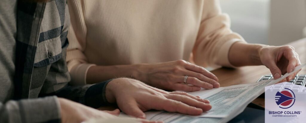 A man and woman sit at a bench with a laptop assessing paperwork together.